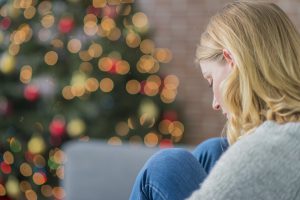 Woman looking sad in front of a Christmas tree.