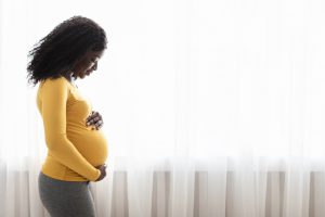 A pregnant Black mother looks down at her stomach.