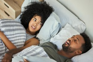 A woman giving a frustrated look to a snoring man next to her in bed.