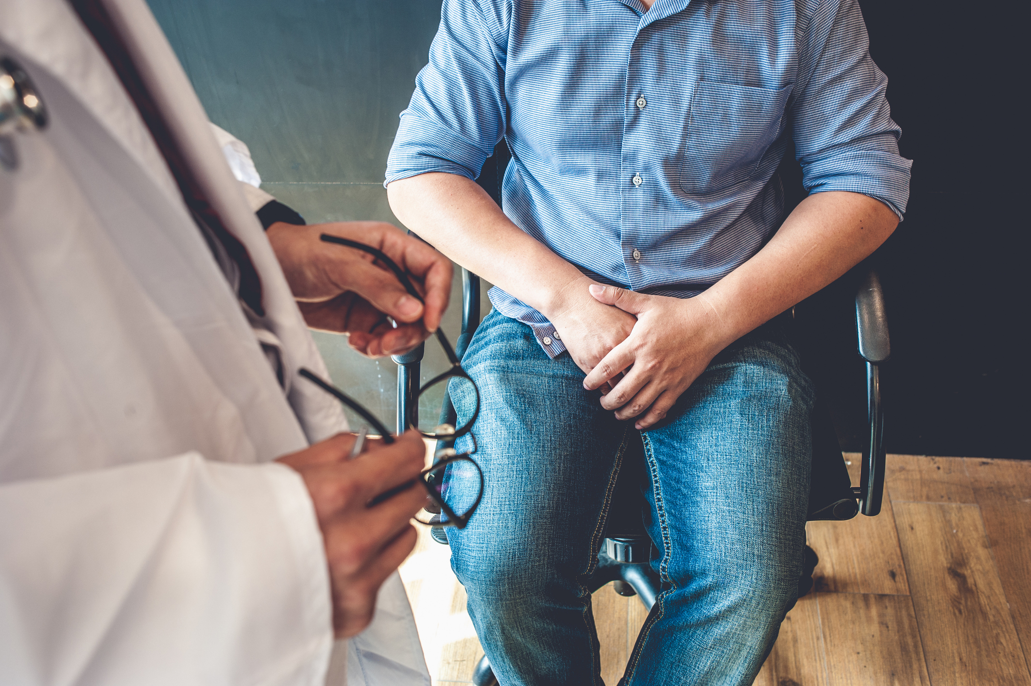 Doctors are consulting with young men about prostate cancer and venereal disease, including sexual dysfunction.Men Health Concept A doctor holding a pair of glasses looking down at a man sitting in a chair.