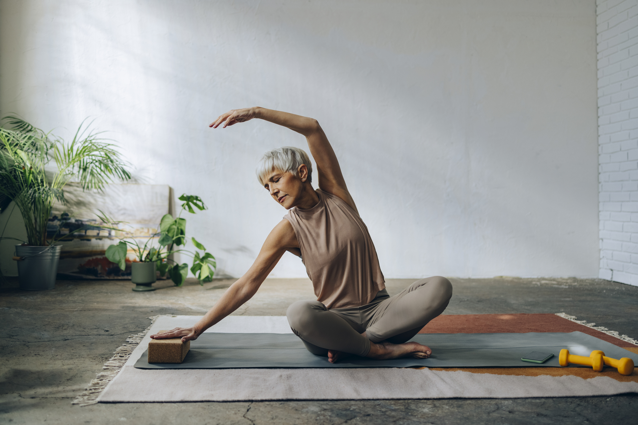 Senior Woman Doing Home Workout Training Serious woman in sportswear sitting on a exercise mat and stretching arms.