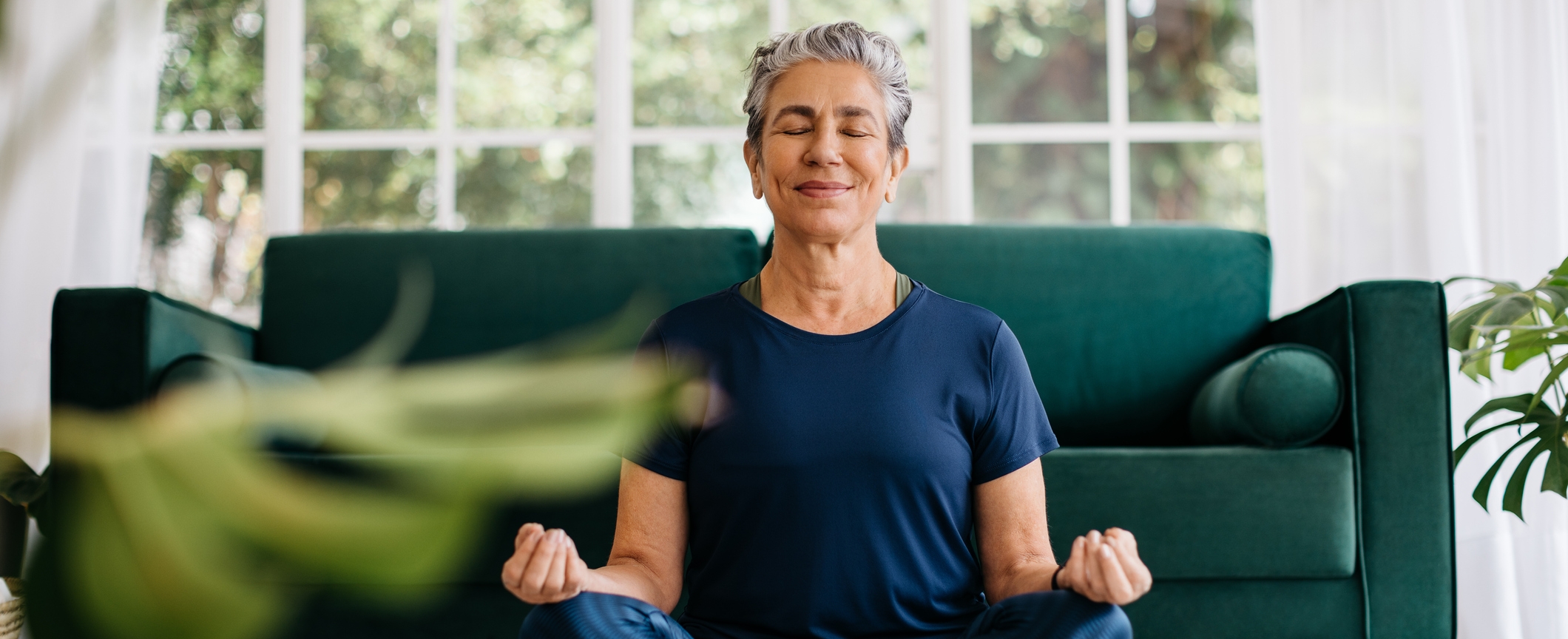 Relaxing the mind and finding inner peace with yoga: Senior woman meditating at home Senior woman meditating in lotus position at home, sitting on the floor in fitness clothing. Mature woman doing a breathing workout to achieve relaxation, peace and mindfulness.