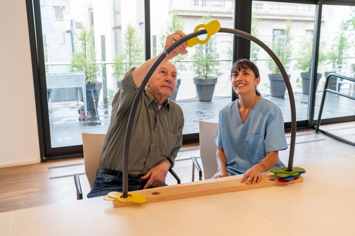 Senior male patient moving pieces from one side to another through a tube in occupational therapy with a cheerful Latin American therapist - Healthcare concepts